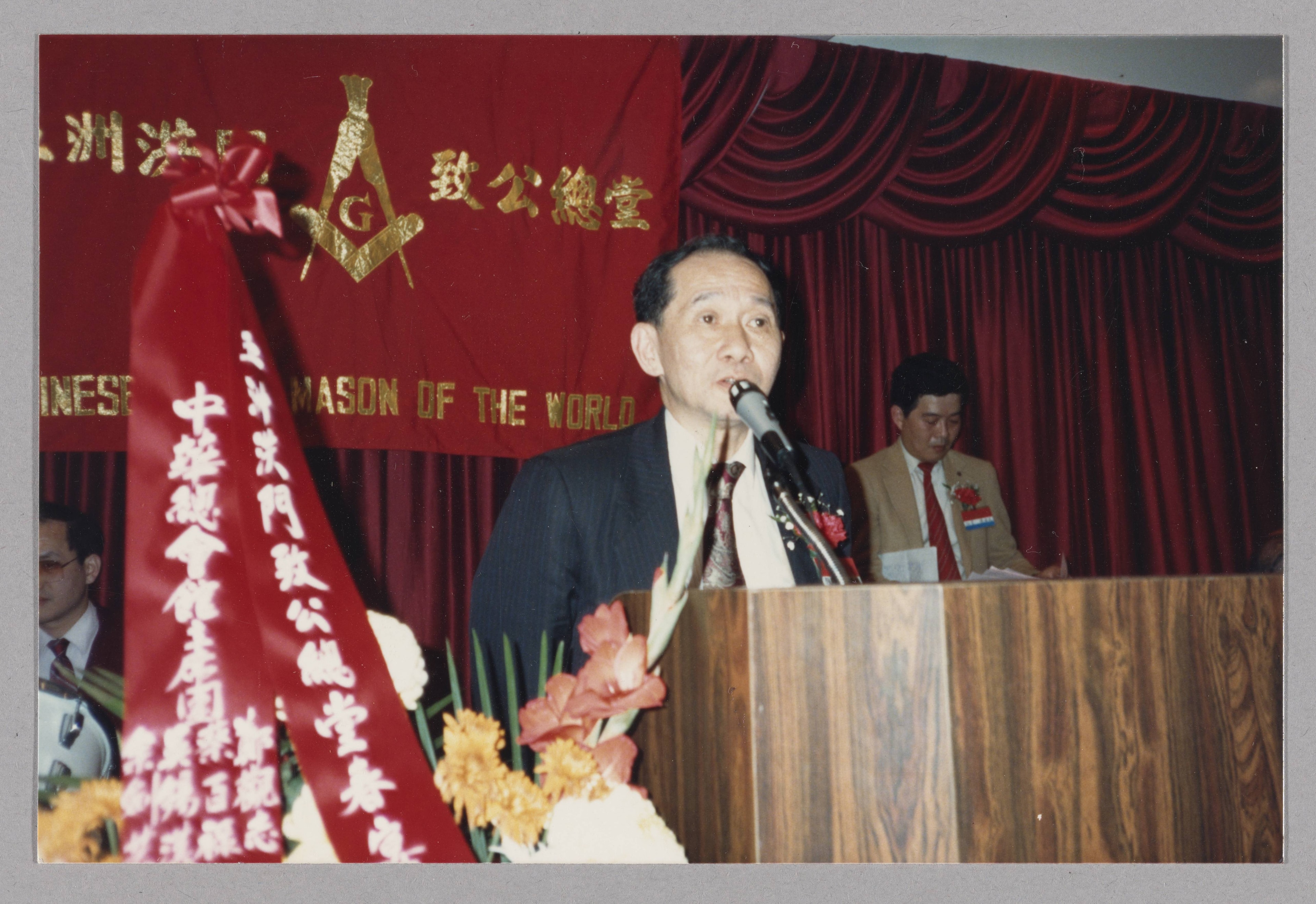 Supreme Lodge spring banquet (五洲洪門致公總堂春宴). Speaker at podium before the lodge banner. This is an archival photograph of a past event; the individual pictured is not identified.